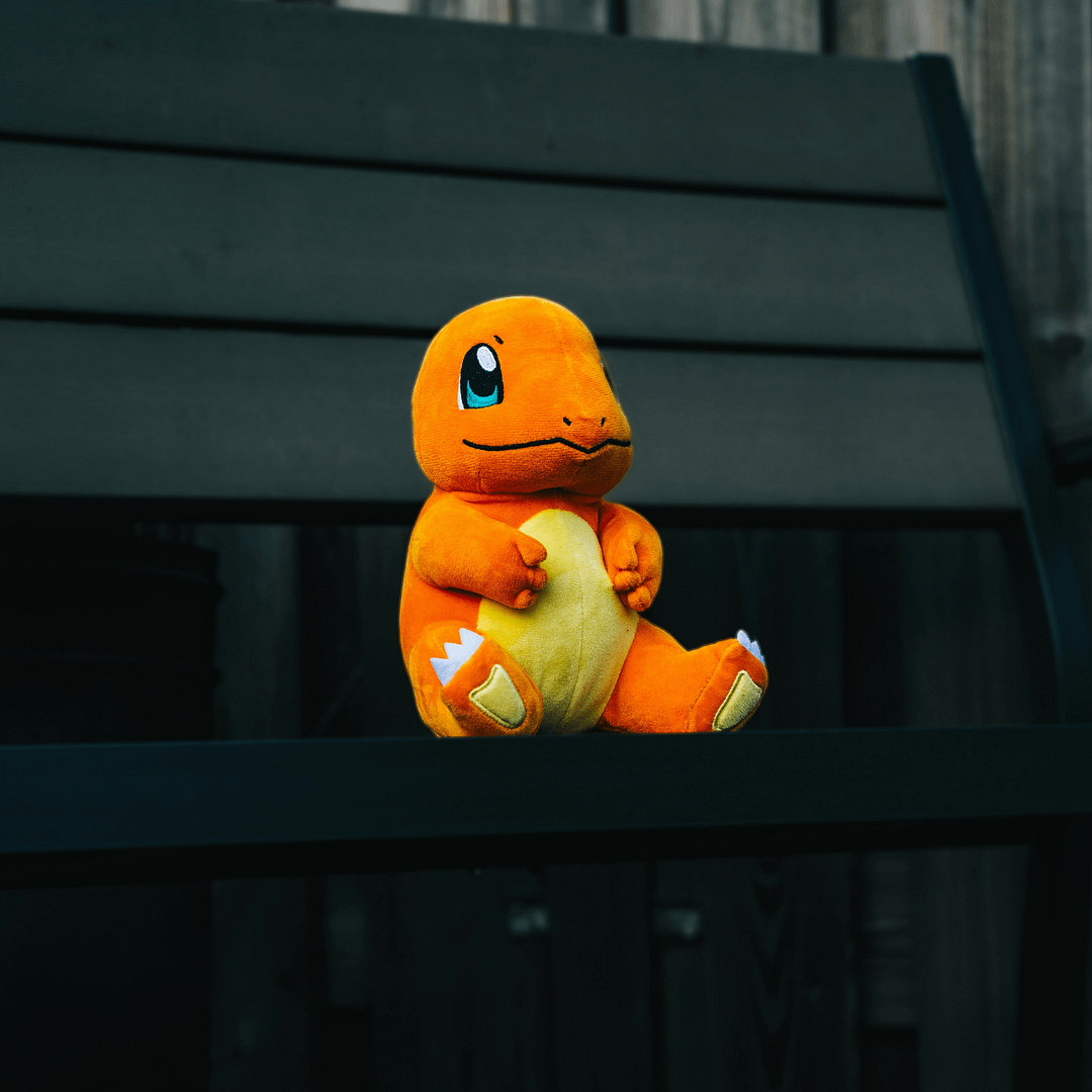 A plush toy of Charmander, one of the most iconic Pokémon, sitting on a dark wooden bench. Symbolizing digital collectibles, AR gamification, and the psychology of collection that makes Pokémon Go such an addictive digital experience.